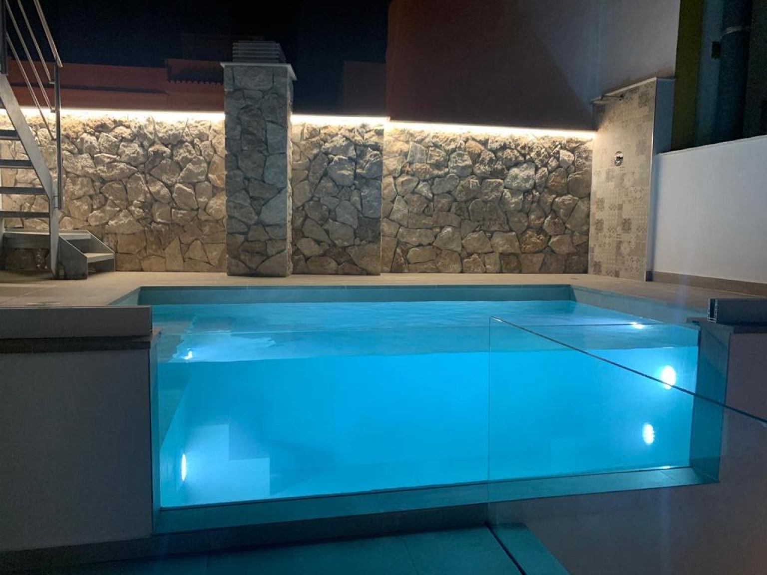 ILUMINACIÓN DE PISCINA DE CRISTAL Y PARED DE PIEDRA